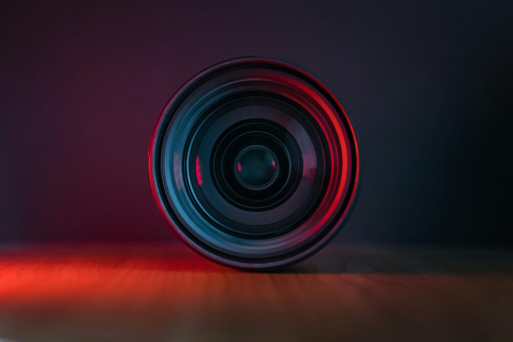 Close-up of a camera lens on a wooden surface with vivid red lighting.