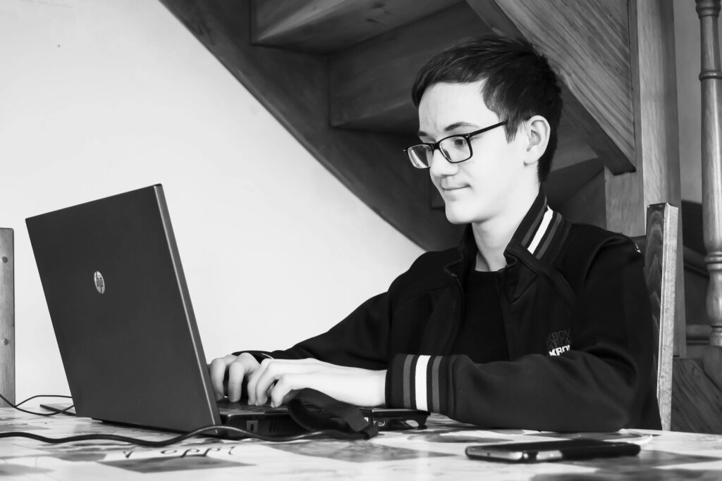 Teenage boy working on a laptop at home, focused and productive in a black and white setting.