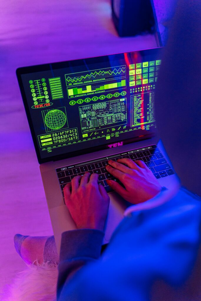 Les métiers de l’informatique les plus demandés en Algérie en 2025 An unrecognizable person using a laptop indoors with digital screens displaying data and analytics.