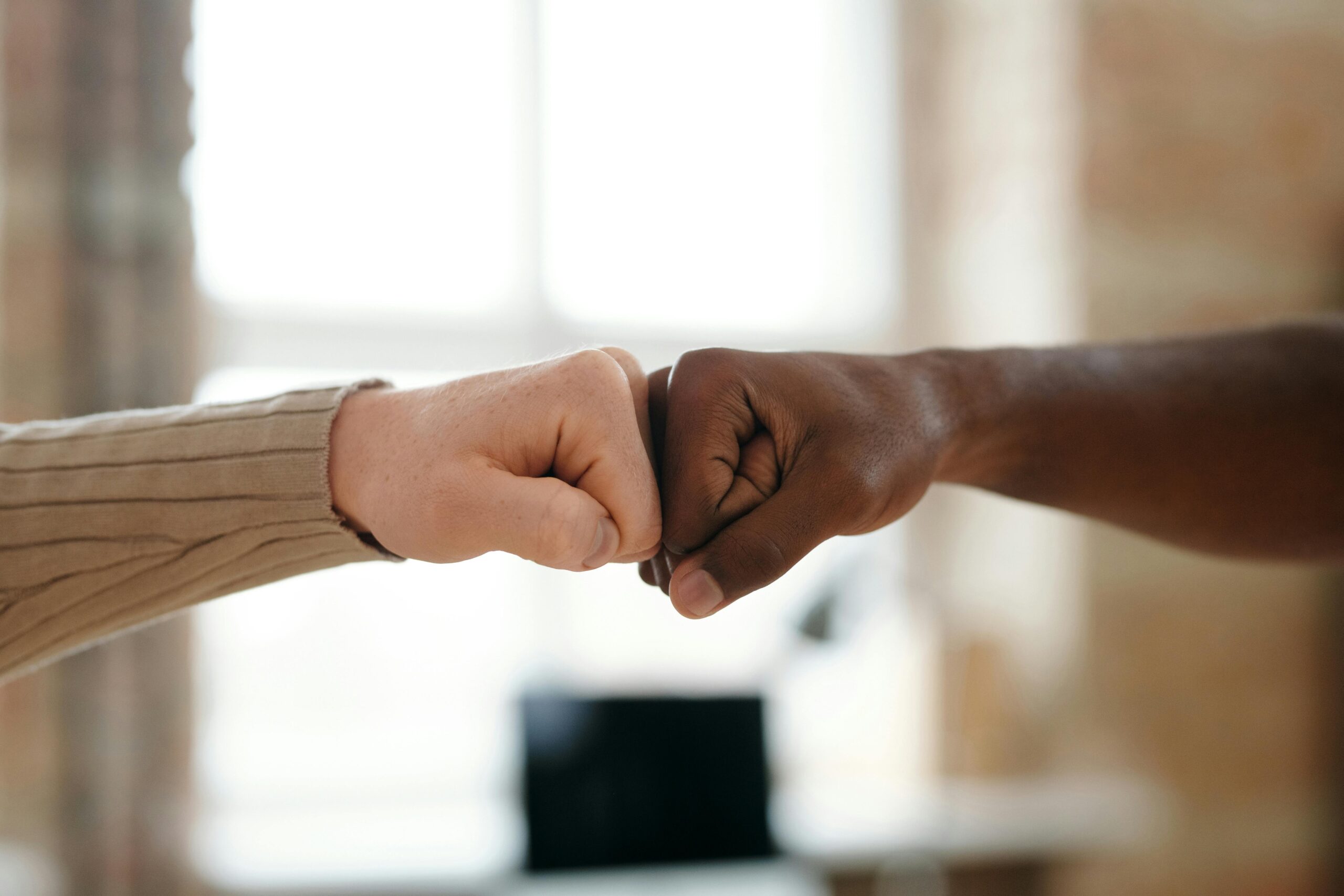 About A close-up image showing two diverse hands in a fist bump, symbolizing unity and teamwork.