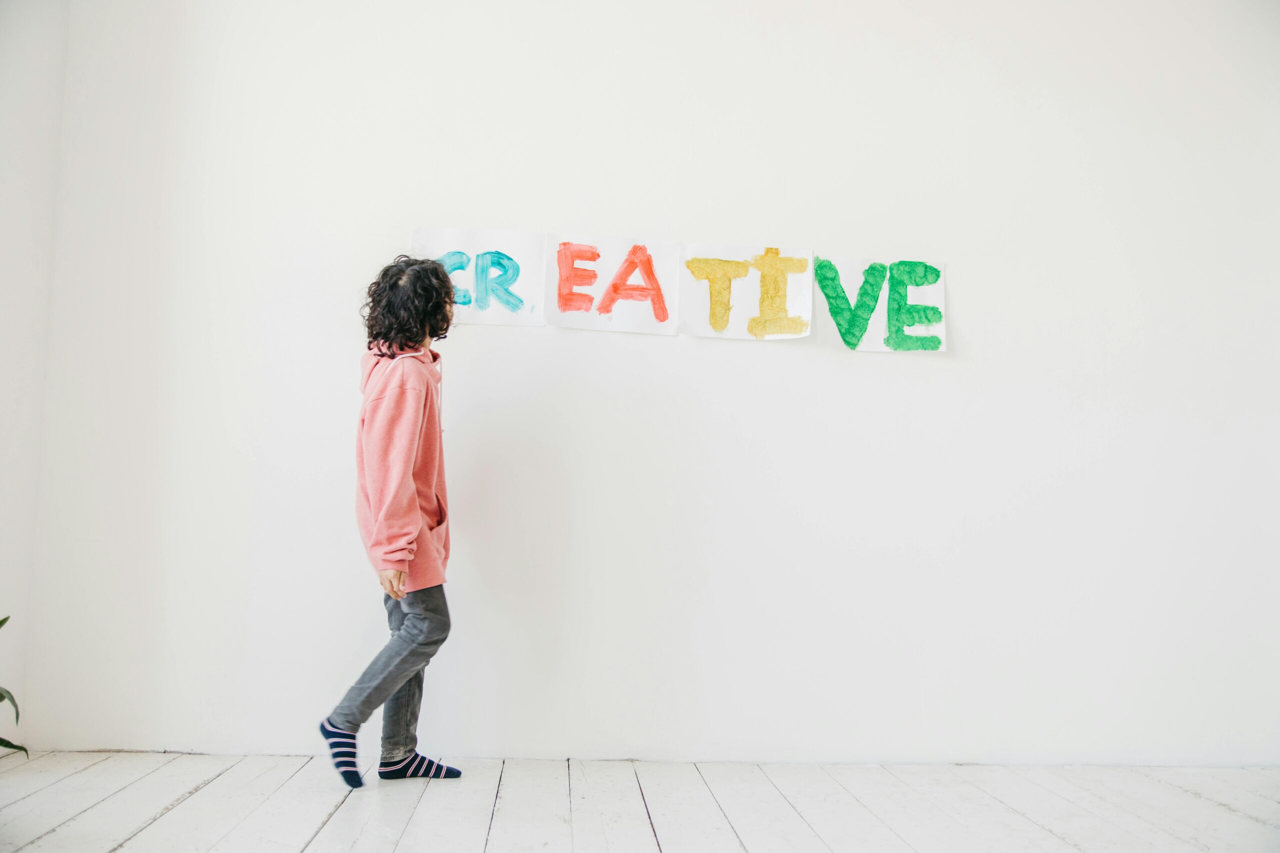 About A child in casual attire creatively paints on a white wall indoors, spelling