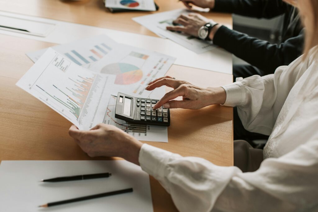 Pourquoi étudier le management est un avantage pour votre avenir professionnel ? Hands performing financial calculations with charts and a calculator at a meeting table.