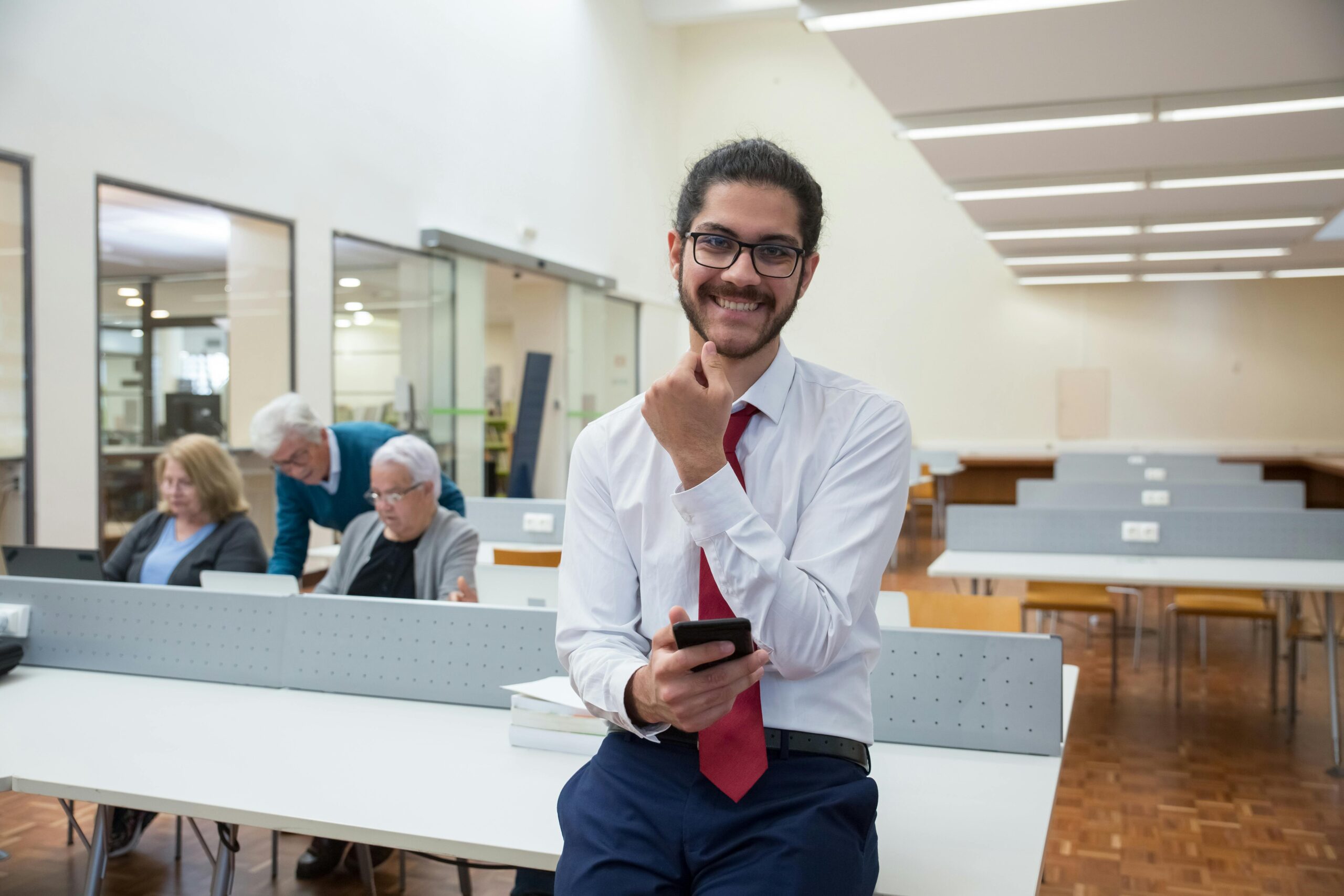 Young man in a professional setting with a mobile phone, smiling and relaxed.